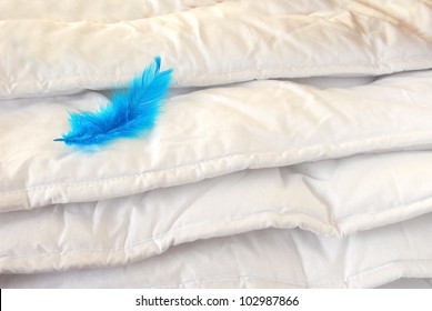 White Folded Cotton Duvet Background With Blue Feather