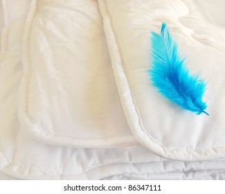 White Folded Cotton Duvet Background With Blue Feather