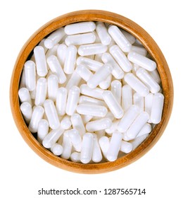 White food supplement capsules in wooden bowl. Hard shelled capsules, filled with powder, for example vitamin B12, cobalamin. Isolated macro food photo, closeup, from above, on white background.