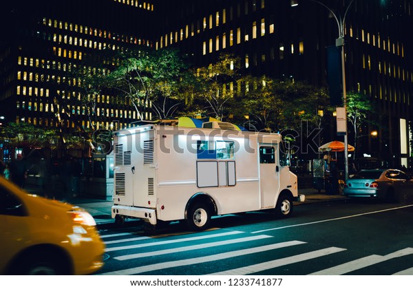 White food truck parked on city street near\
buildings using for retail business startup, Van automobile with\
mock up copy space area for brand name selling ice cream parked in\
urban setting at night