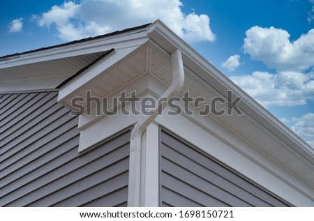 White frame gutter guard system, with gray horizontal vinyl siding fascia, drip edge, soffit, on a pitched roof attic at a luxury American single family home neighborhood USA
