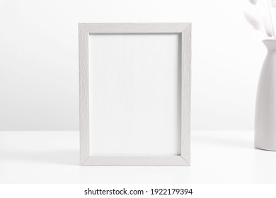 White frame mockup with dried flowers lagurus in vase on white table. Front view. Place for text, copy space, mockup