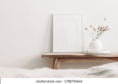 White frame mockup on vintage wooden bench, table. Modern white ceramic vase with dry Lagurus ovatus grass and marble tray. Blurred beige linen blanket in front, Scandinavian interior.
