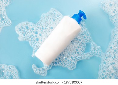 White Free Shampoo Bottle In The Water With Soap Bubbles, 
Lather And Water Droplets. Top View On Blue Background