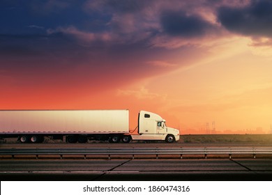 White freight truck driving on freeway road under red sunset sky.
