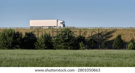 White freight truck on an elevated road above green fields and trees, useful for logistics, road cargo transport and supply chain themes.