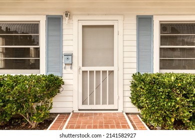 White Front Door Of A House That Is Surrounded By A White Picket Fence And Elegant Landscaping.