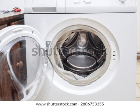 White front loading washing machine with door open showing empty broken metal drum, home appliance repair and maintenance 