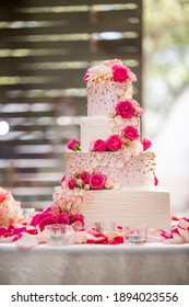 White Frosting Four Tiered Wedding Cake Decorated With Pink Roses On A White Table For A Nuptial Ceremony