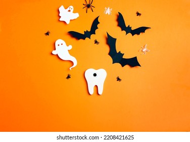 White funny creepy tooth with Halloween decorations on orange background. Dentist Halloween concept. Top view, flat lay.