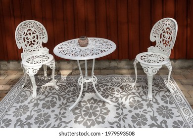 White Furniture Table And Chairs. Beautiful White Metal Outdoor Furniture. Garden Design. Carved Table And Chairs With Patterns For Relaxing In The Courtyard Of A Villa Or Cottage. Glass Candlestick.