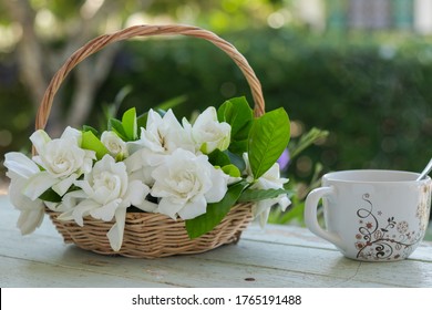 White Gardenia Bouquet In The Wicker Basket And White Cup Of Coffee That All Of Them Put On The Wooden Table In The Home Garden.