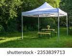 White gazebo or pavilion with a wooden table, benches and a flower bouquet on the meadow in a natural garden, idyllic summer place gives protection from sun and rain, copy space, selected focus