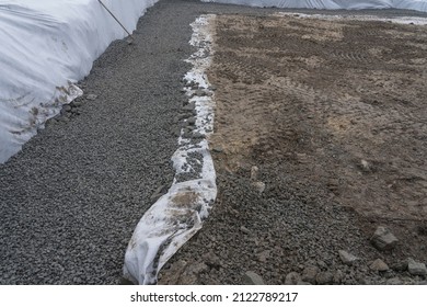 White Geotextile Layer Between Gray Raw Stones Gravel And Black Ground. Making Place For Parking And Beton Construction.