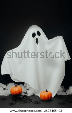 A white ghost character is floating with orange pumpkins and black spiders on a dark background