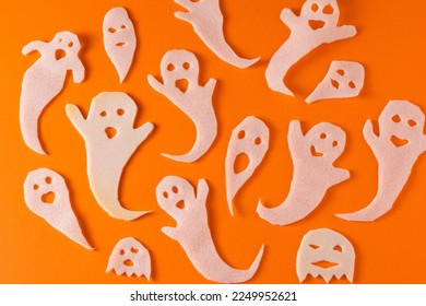 White ghosts kids craft for Halloween. Paper ghost on orange background top view. A scary and funny monster toy. Cartoon creepy Whisper. DIY hand made. Set boo characters Spooky halloween ghost