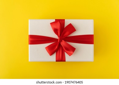 White Gift Box With Red Ribbon. Presentation On Yellow Background Top View