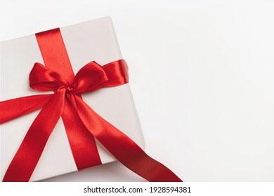 White gift box with red ribbon bow on light background. Christmas, new year, birthday, anniversary or sale background. Top view, flat lay, copy space, template for design
