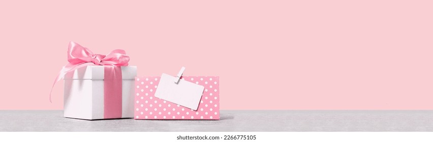 White gift box with shining pink ribbon bow on pink background with mockup gift card. Gift or holiday concept. Mothers Day, birthday wedding or St Valentines day banner with copy space