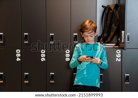 White ginger boy using mobile phone in checkroom at school