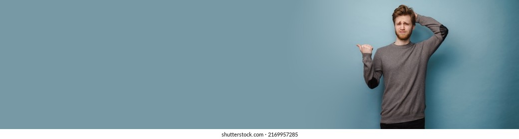 White ginger man with beard frowning and pointing finger aside isolated over blue background - Shutterstock ID 2169957285