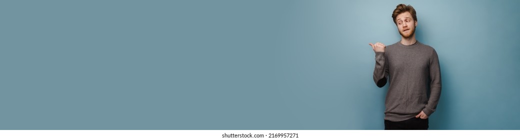 White ginger man pointing finger and looking aside isolated over blue background - Shutterstock ID 2169957271