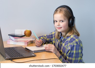 White girl 10 years old studying online at home. Headphones, laptop, smartphone. Checkered shirt. Gray background. Selective focus
