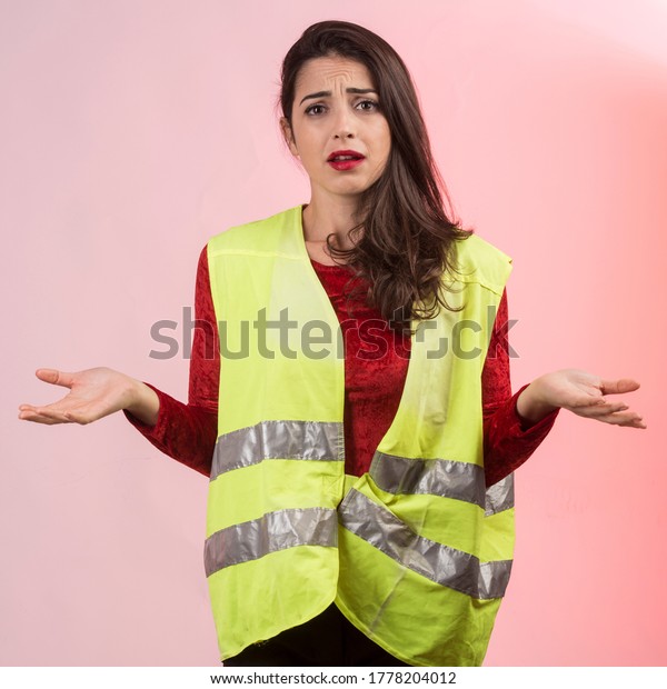 white girl with dark hair and a yellow\
emergency vest on her is desperate after committing an accident,\
isolated on pink\
background\
