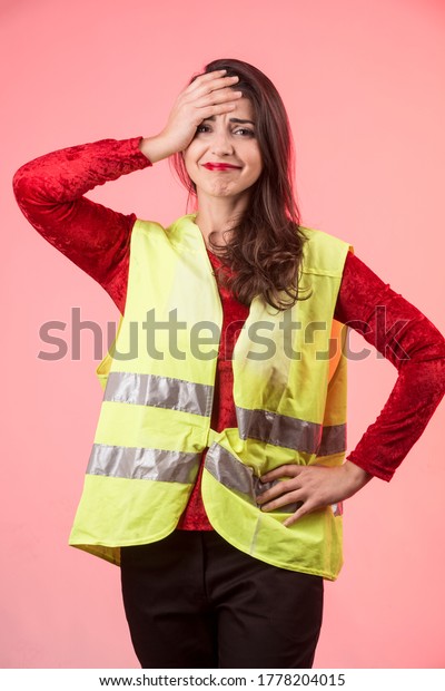 white girl with dark hair and a yellow
emergency vest on her is desperate after committing an accident,
isolated on pink
background

