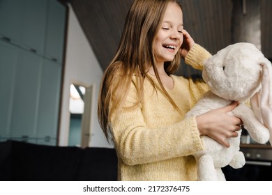 White Girl Laughing While Standing With Her Toy Bunny At Home