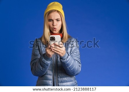 White girl wearing hat frowning and using mobile phone isolated over blue background