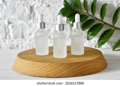 White glass cosmetic bottles pipette with green leavers on a wood stand on a white wall background. Top view. SPA natural organic cosmetics set. Skincare concept. Copy space.