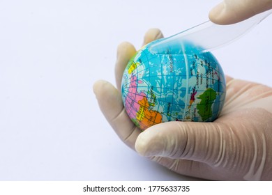 White Gloved Hand Holds A Blue Globe And A Clear Plastic Knife. Person Hand Is Holding The Knife And Slash It Onto The Ball. Humans Are About To Kill The World With A Lot Of Plastic Waste.