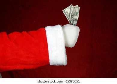 A White Gloved Santa Arm Holds A Fist Full Of Cash Against A Crushed Red Velvet Background