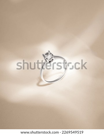 White gold ring with diamond on beige background with shadows. Still life and creative photo