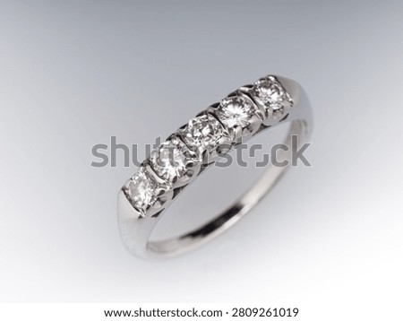 A white gold ring with five round cut diamonds arranged in a row, viewed from an angle against a white background.