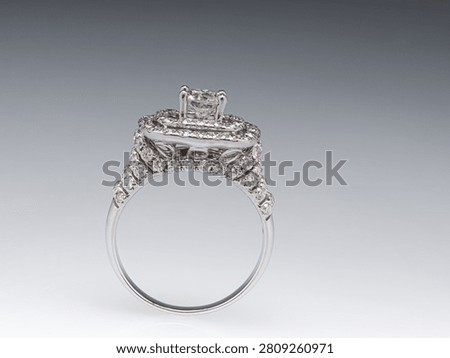 A white gold ring with a rectangular double halo of diamonds and a diamond-encrusted band, shown on a light background.