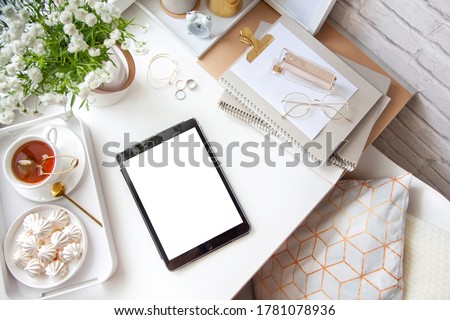 White and gold stationery at the female workplace. Jewelry, bracelets and rings. Flowers in a vase, tea and bizet. Alarm clock and pig piggy bank. Stylized women's desk, office desk.