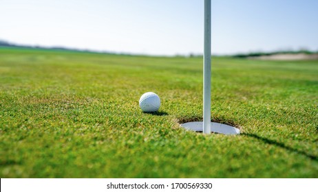 White Golf Ball Laying On Green Grass Of Play Field On Sunny Day With Cloudy Sky Above