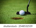 White golf ball near a hole with a black putter on a green field, close-up view, clear focus, professional golfing equipment, outdoor sports concept