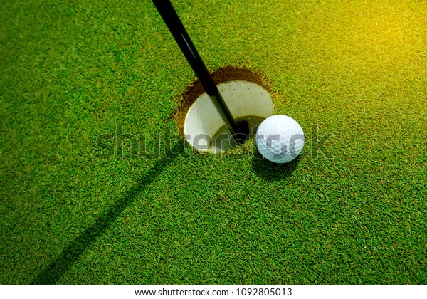 White golf ball near the hole on the green grass\
at summer - leisure\
activity