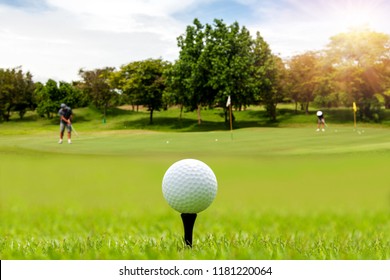 White Golf ball on tee ready to be shot on blurred beautiful landscape of golf course in bright day time with golfer playing golf on course. Sport, Recreation, Relax in holiday concept.	