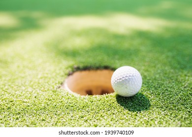 A white golf ball is placed in the mouth of the hole on the green grass.