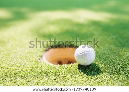 A white golf ball is placed in the mouth of the hole on the green grass.