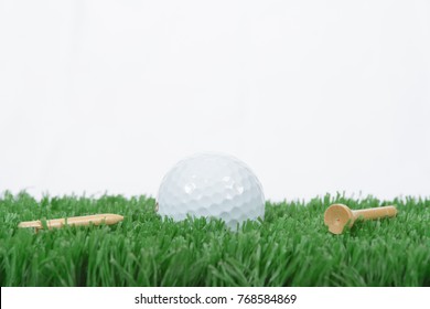 A White Golf Ball Sitting On The Green Rough Grass With A White Background And A Broken Tee.