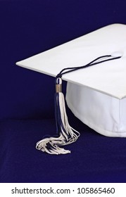 White Graduation Cap On Royal Blue Background With Tassel