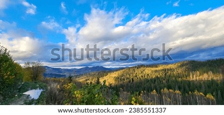 White and gray cumulus, stratus, cirrus clouds over the mountains. Autumn nature, yellow leaves on the trees. Panorama of the majestic mountains. Real nature.