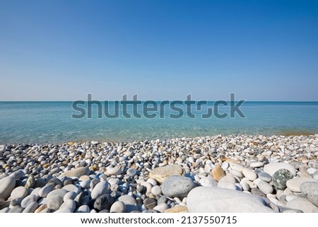 White and gray stones softly rounded and washed from sea water with horizon over the sea and cloudless sky 