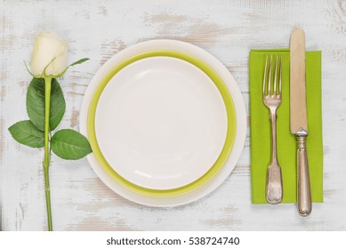 White And Green Empty Plates, Green Linen Napkin, Old Fork And Knife And White Rose Flower On An Old Wooden Table; Top View, Flat Lay, Overhead View