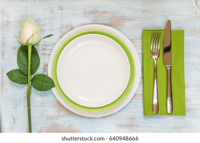 White And Green Empty Plates, Green Linen Napkin, Fork And Knife And White Rose Flower On An Old Wooden Table; Top View, Flat Lay, Overhead View